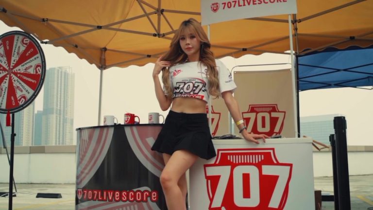 707Livescore booth with a model, branded counter, mugs and prize wheel under a yellow canopy at MyTown